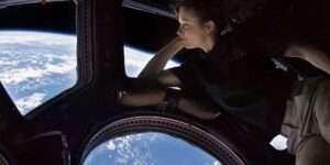 Photo of a young woman looking at the Earth through a window on the space station