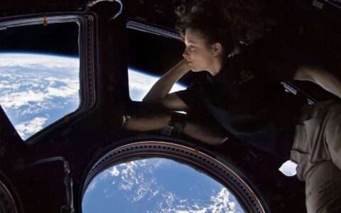 Photo of a young woman looking at the Earth through a window on the space station