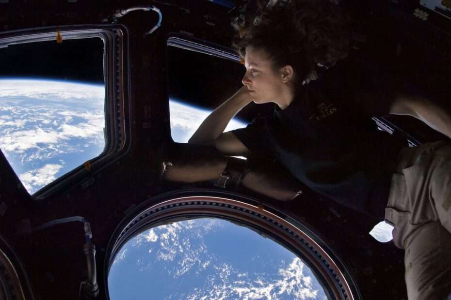 Photo of a young woman looking at the Earth through a window on the space station
