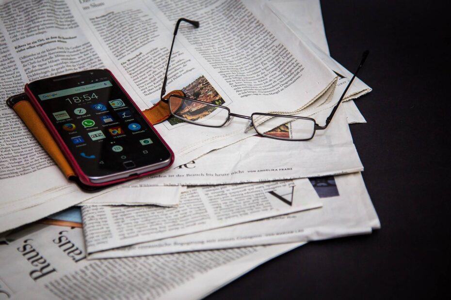 Photo of a newspaper, phone and reading glasses